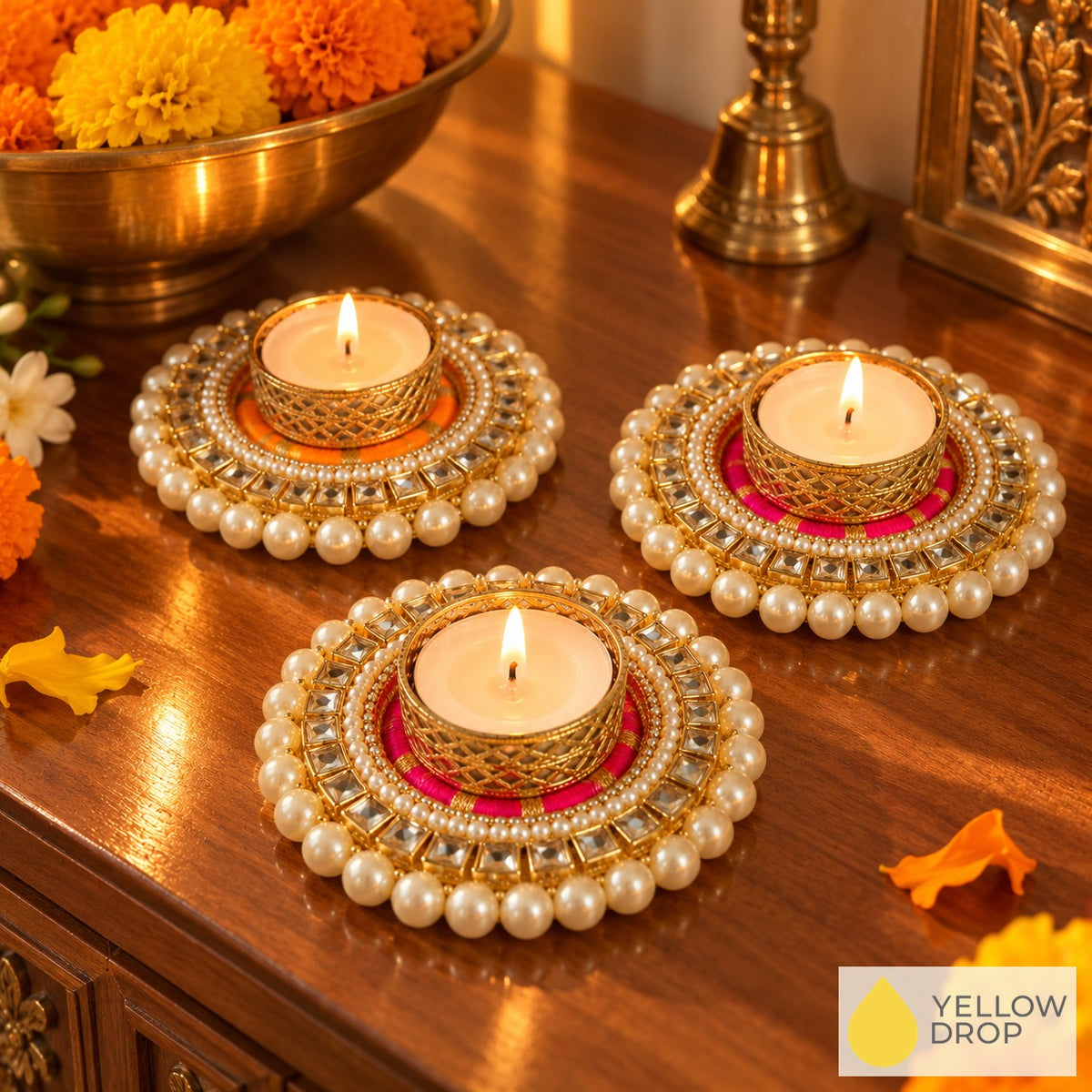 Three Kundan Pearl tealight holders lit on a wooden console with a brass bowl of marigolds